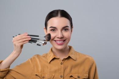 Photo of Happy woman with different makeup brushes on light grey background