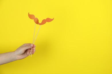 Photo of Woman with fake paper mustaches on yellow background, closeup. Space for text