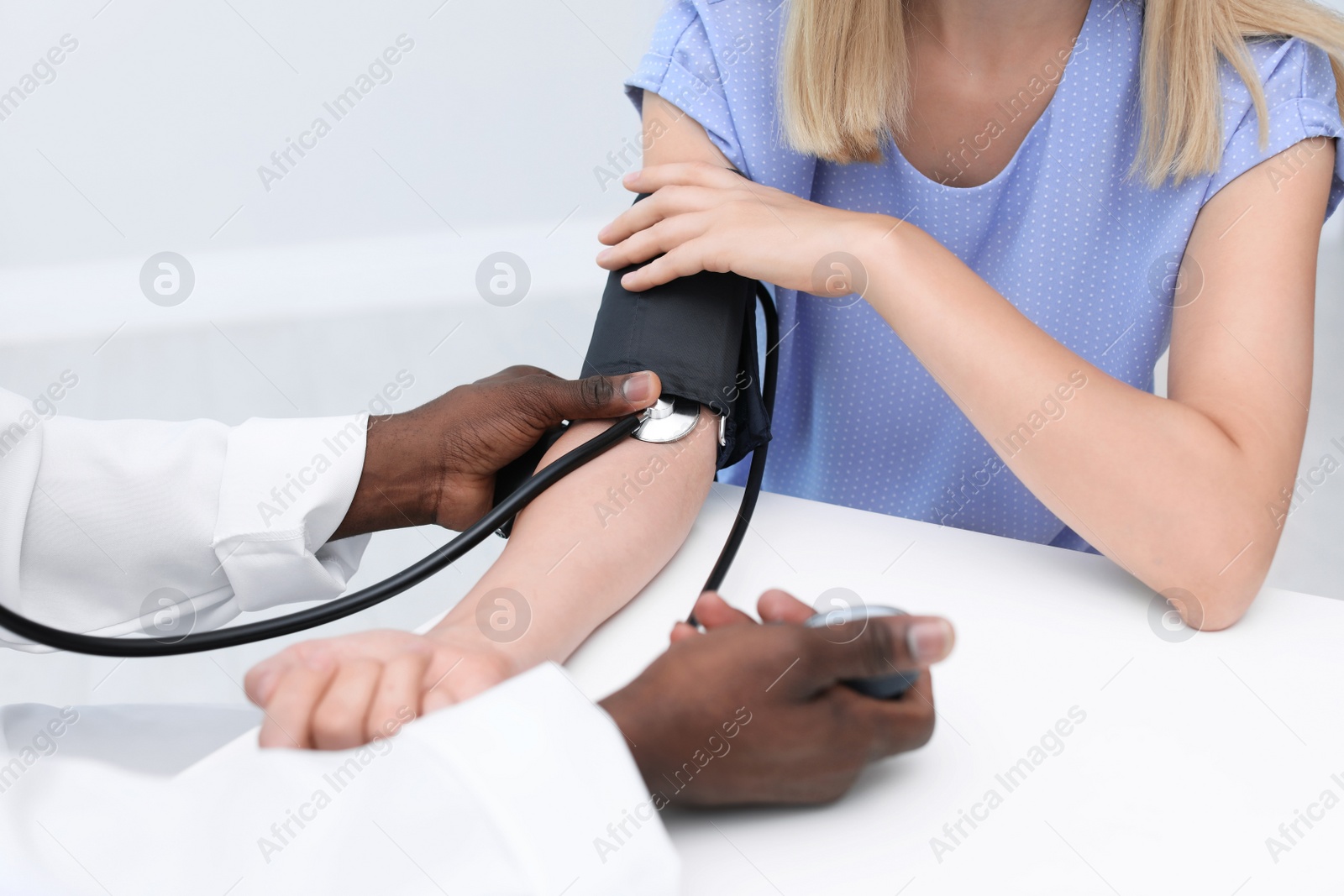 Photo of Young African-American doctor checking patient's pulse and blood pressure in hospital