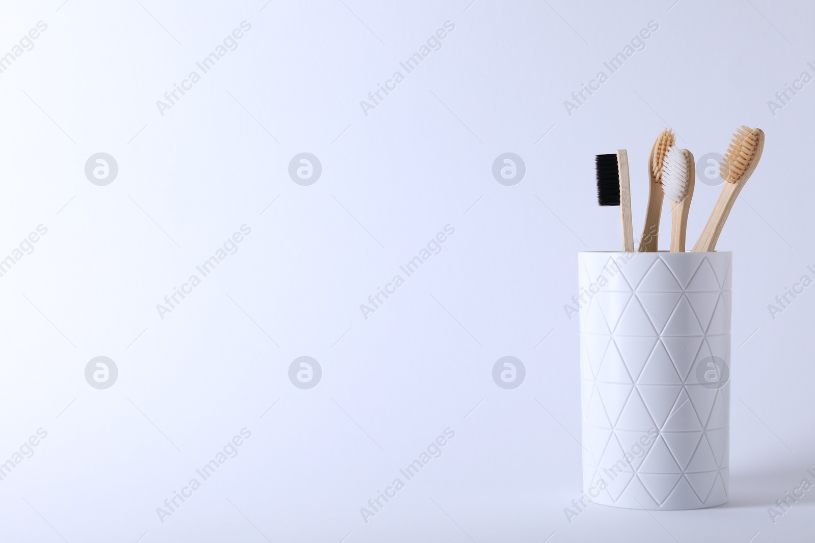 Photo of Bamboo toothbrushes in holder on white background, space for text