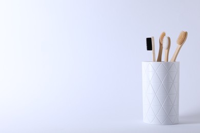 Photo of Bamboo toothbrushes in holder on white background, space for text