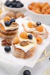 Photo of Tasty sandwiches with brie cheese, fresh berries and walnuts on white table, closeup