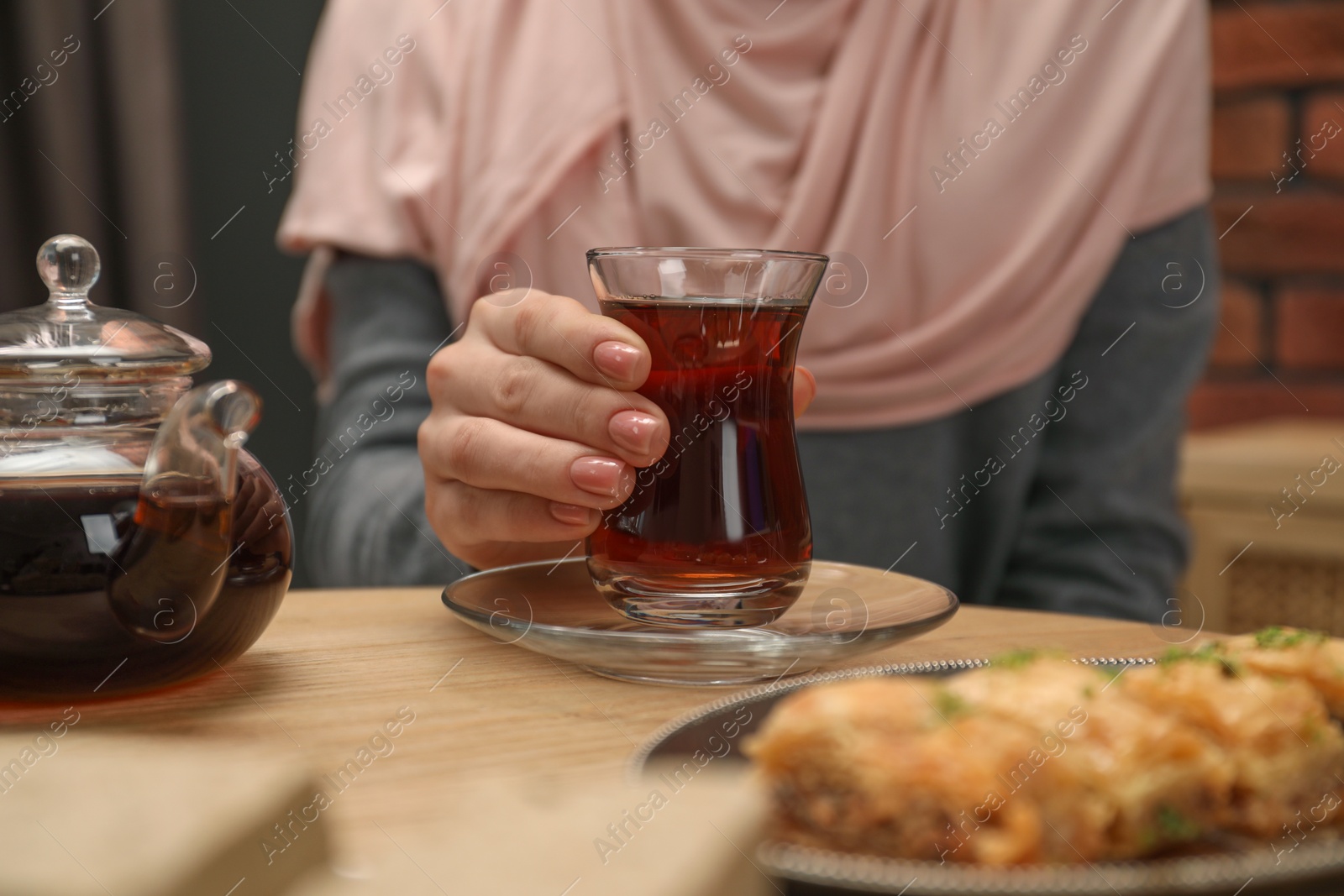 Photo of Woman with cup of delicious Turkish tea at wooden table, closeup