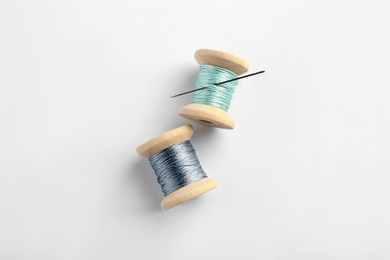 Colorful sewing threads with needle on white background, top view