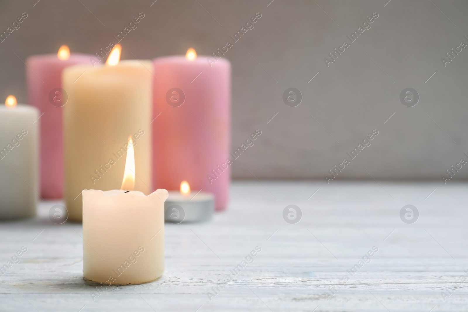 Photo of Different wax candles burning on table against light background