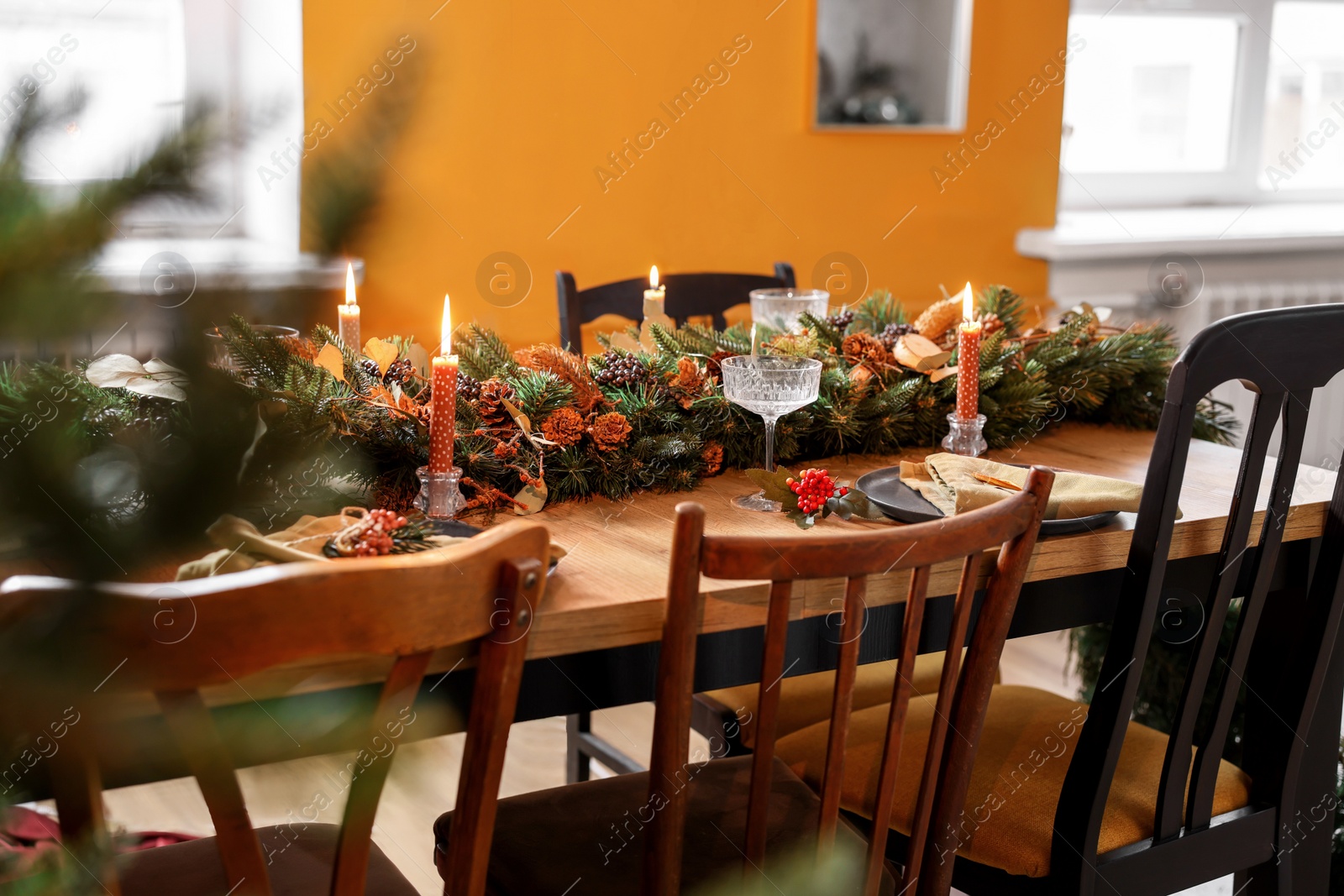 Photo of Wooden table with burning candles and Christmas garland in stylish room. Interior design