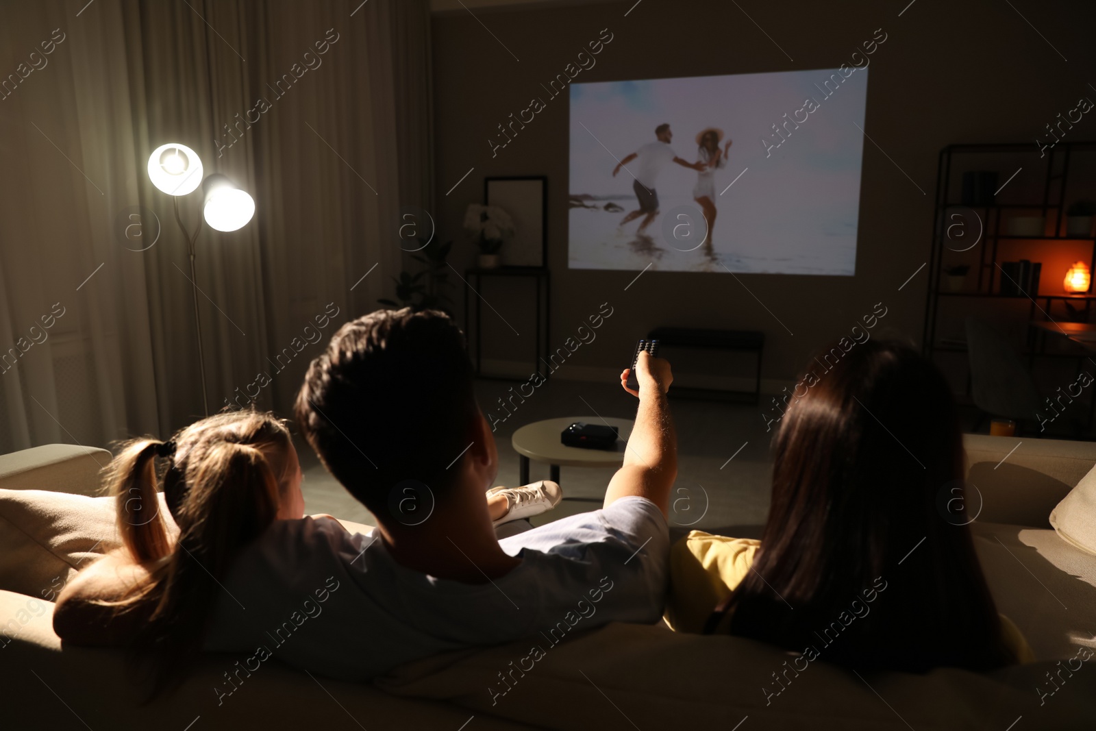 Photo of Family watching movie on sofa at night, back view