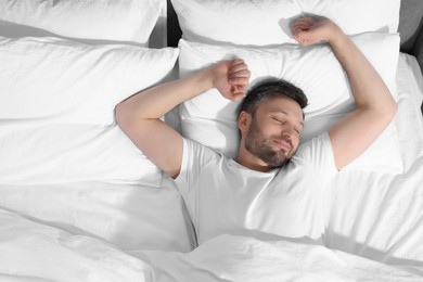 Handsome man sleeping in soft bed, top view