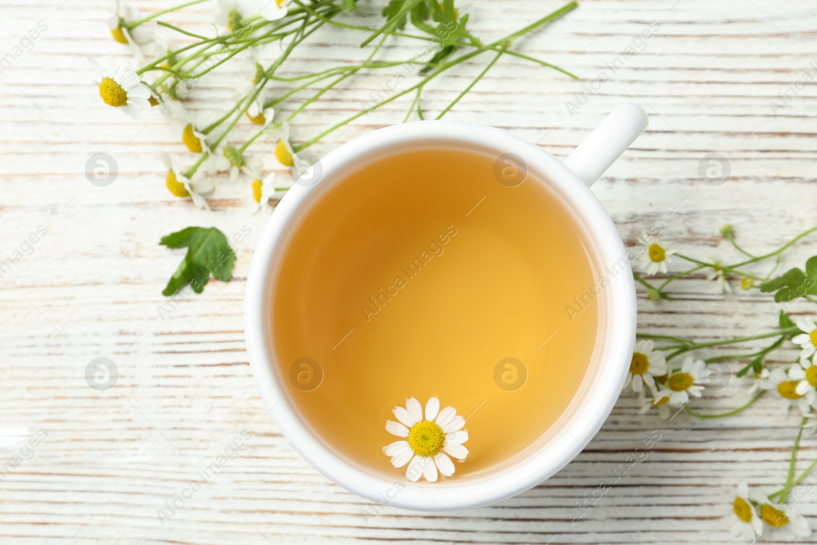 Photo of Cup of tea and chamomile flowers on white wooden table, flat lay