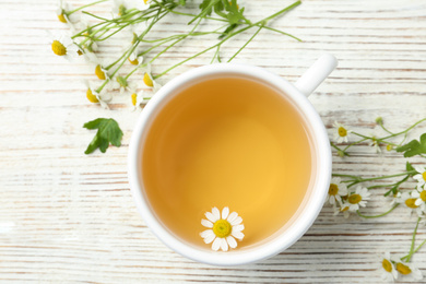 Photo of Cup of tea and chamomile flowers on white wooden table, flat lay