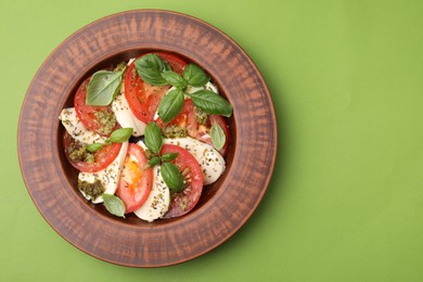 Photo of Plate of delicious Caprese salad with pesto sauce on green table, top view. Space for text