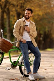 Photo of Young man with bicycle holding takeaway coffee in autumn park