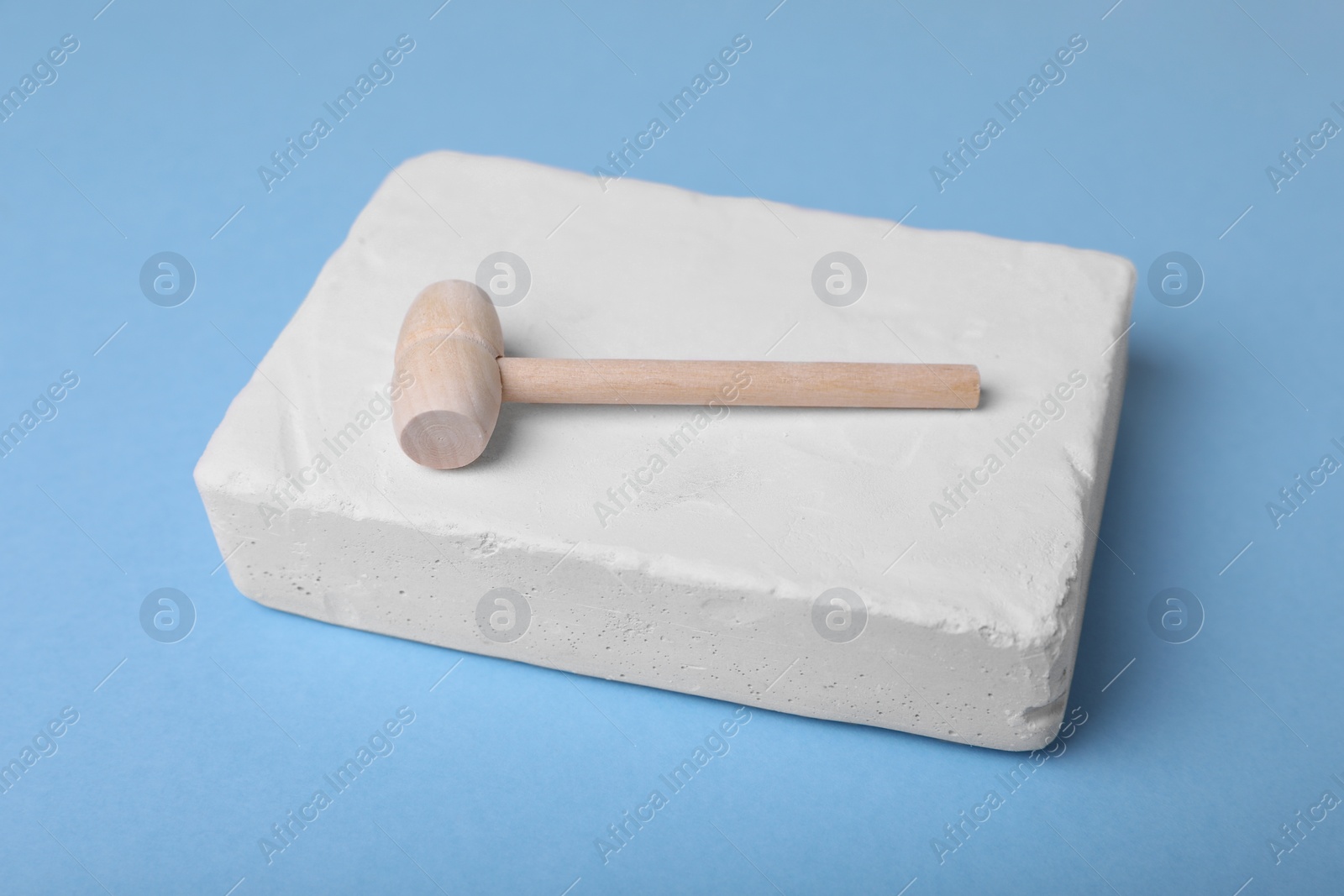 Photo of Educational toy for motor skills development. Excavation kit (plaster and wooden mallet) on light blue background, closeup