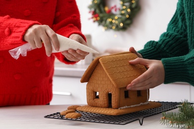 Women making gingerbread house at white table, closeup