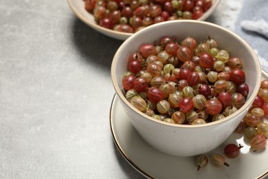 Photo of Fresh ripe gooseberries in bowls on light grey table. Space for text