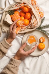 Woman with delicious ripe tangerines and glass of sparkling wine on white bedsheet, top view