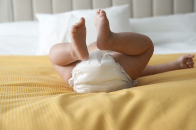 Photo of Cute little baby in diaper on yellow blanket at home, closeup