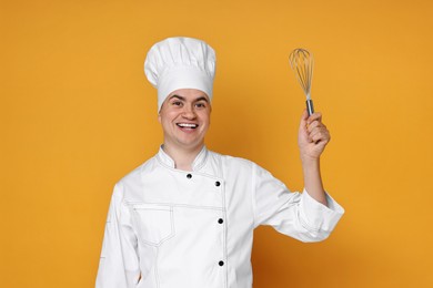 Photo of Portrait of happy confectioner in uniform holding whisk on orange background
