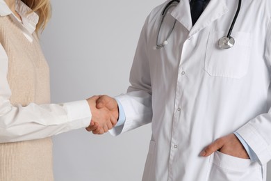 Photo of Doctor and patient shaking hands on light grey background, closeup