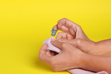 Photo of Woman sewing on fabric with thimble and needle against yellow background, closeup. Space for text