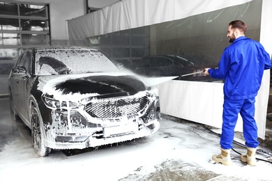 Worker cleaning automobile with high pressure water jet at car wash