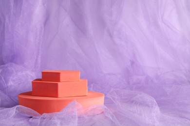 Photo of Orange geometric figures on violet tulle fabric, space for text. Stylish presentation for product