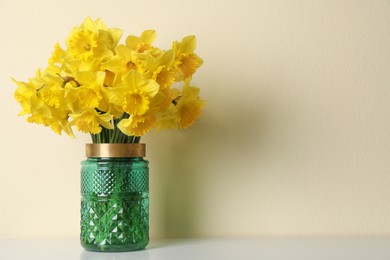 Beautiful daffodils in vase on white table near light wall, space for text