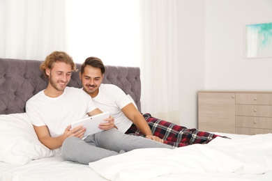 Photo of Happy gay couple with tablet computer on bed at home