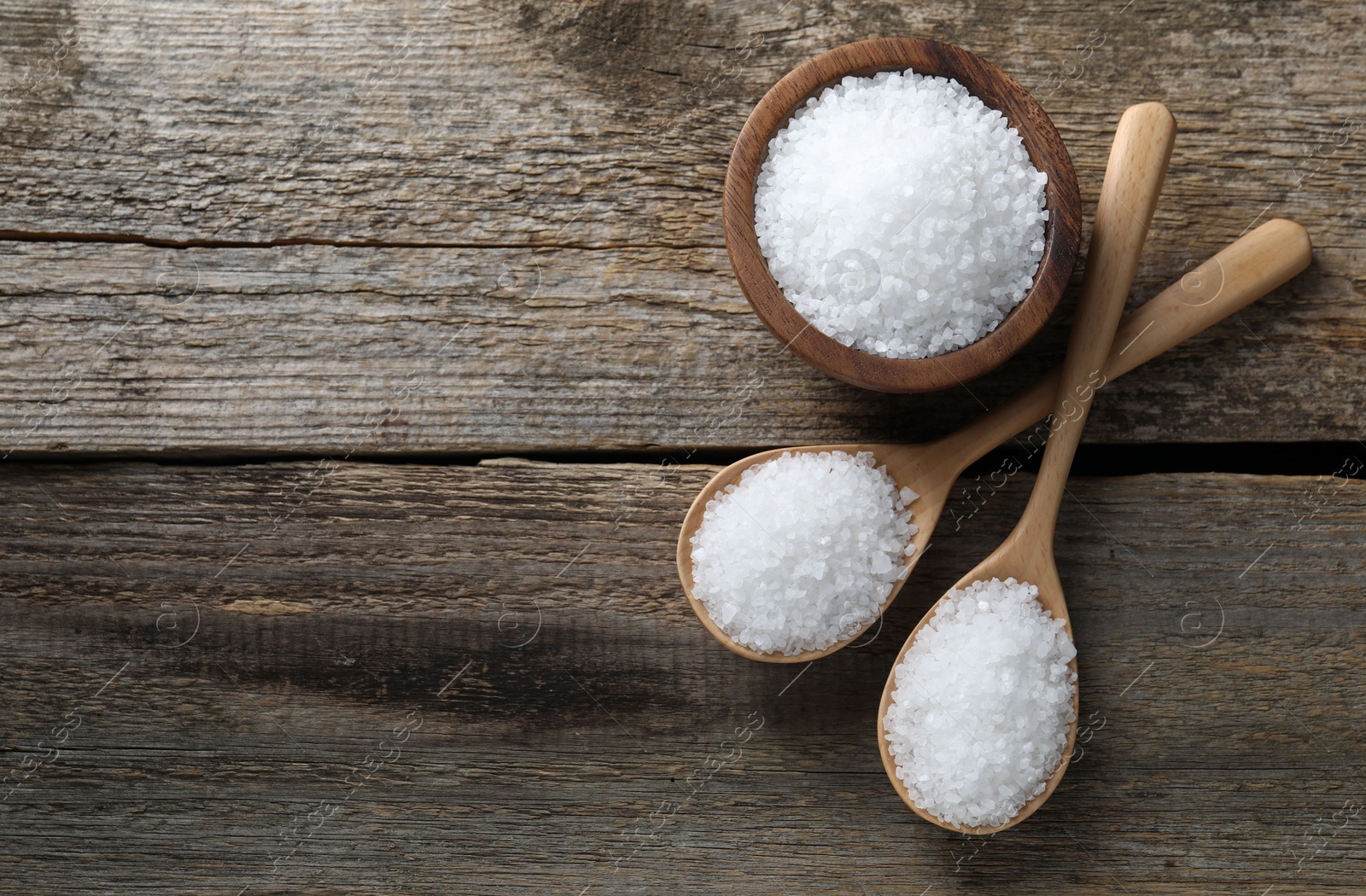 Photo of Organic salt in bowl and spoons on wooden table, flat lay. Space for text