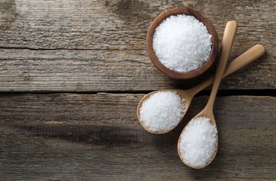 Photo of Organic salt in bowl and spoons on wooden table, flat lay. Space for text