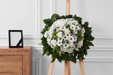 Photo of Wreath of flowers and photo frame with black ribbon on commode in room. Funeral attributes