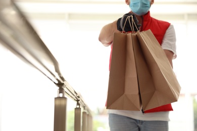 Photo of Courier in protective mask and gloves with order indoors, closeup. Restaurant delivery service during coronavirus quarantine