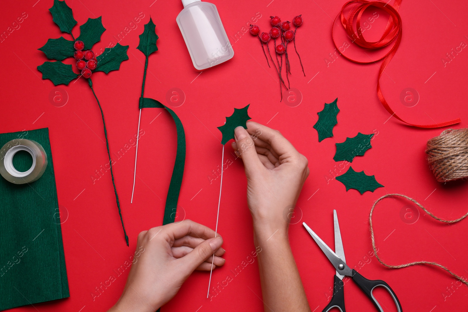 Photo of Woman making mistletoe branch on red background, top view