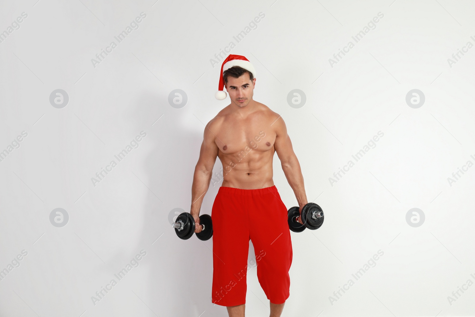 Photo of Sexy shirtless Santa Claus with dumbbells  on light background