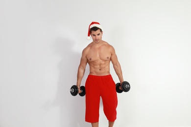 Photo of Sexy shirtless Santa Claus with dumbbells  on light background