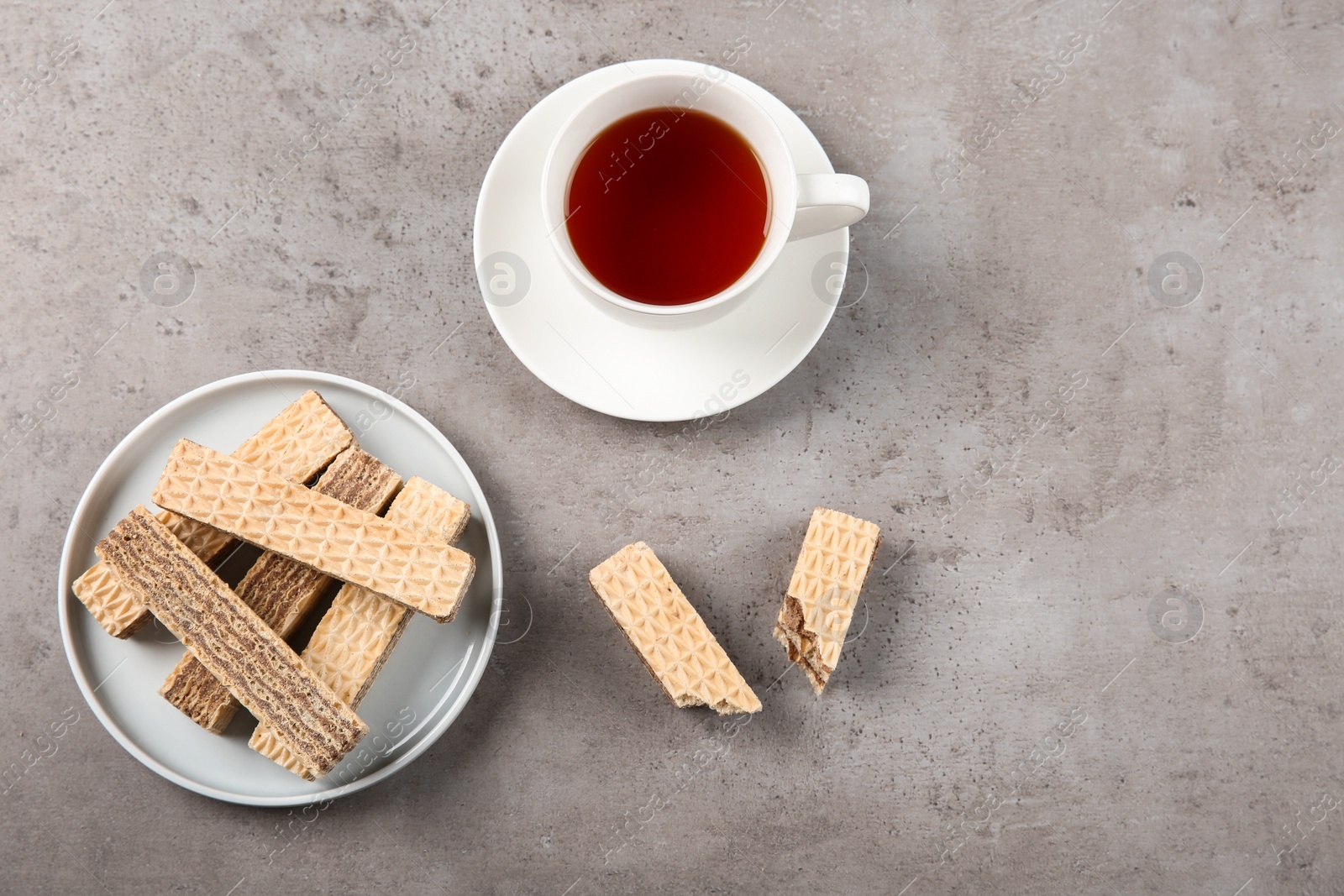 Photo of Plate of delicious wafers with cup of tea on grey stone background, top view. Space for text