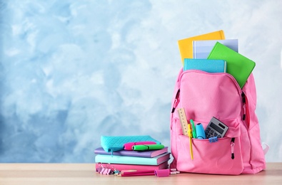 Photo of Backpack with school stationery on table against color background