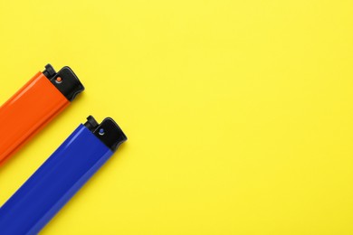 Photo of Stylish small pocket lighters on yellow background, flat lay. Space for text