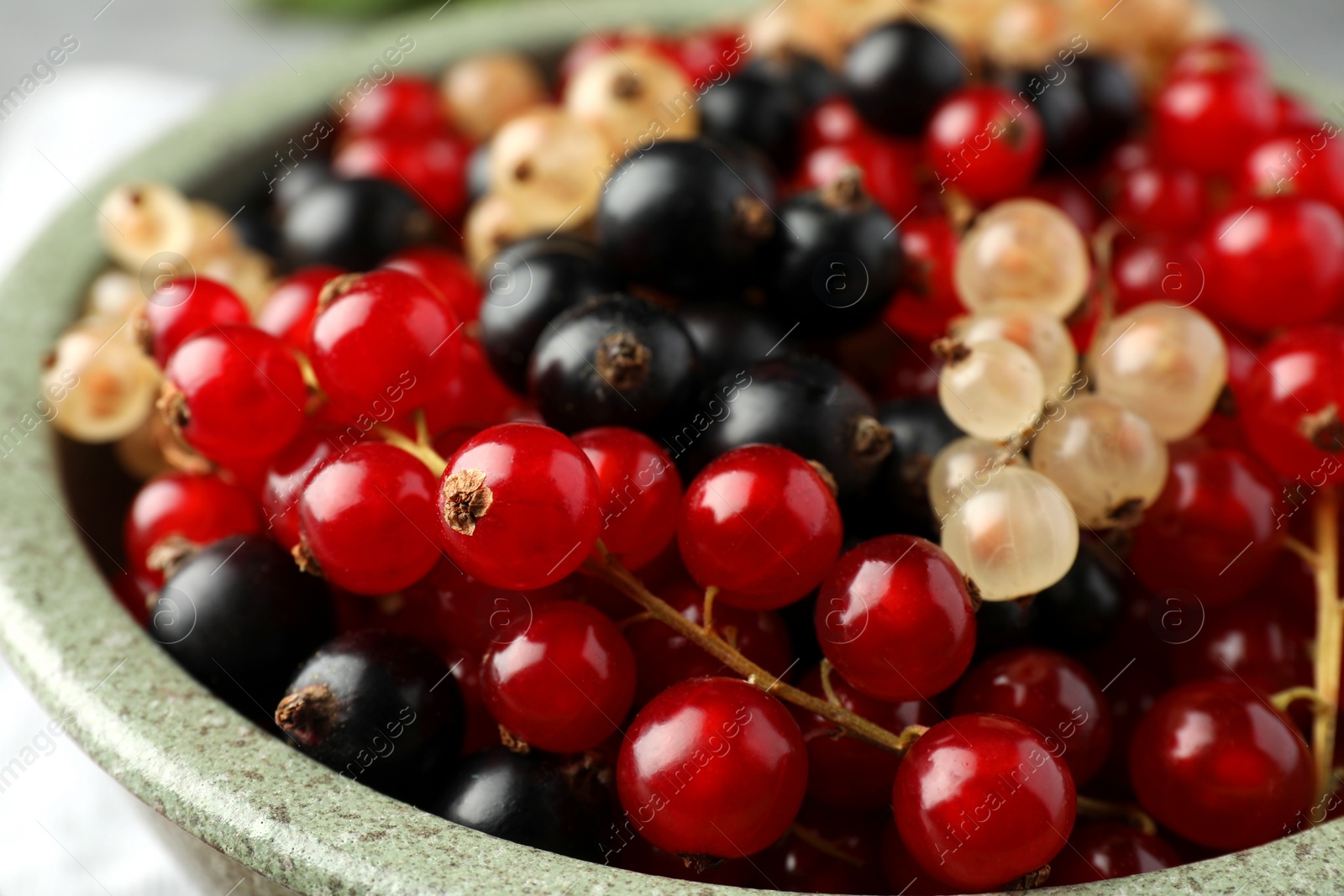 Photo of Different fresh ripe currants in bowl, closeup