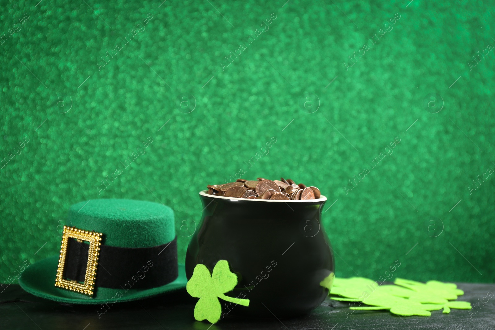 Photo of Pot of gold coins, hat and clover leaves on black stone table against green background, space for text. St. Patrick's Day celebration