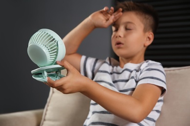 Photo of Little boy with portable fan suffering from heat at home, focus on hand. Summer season