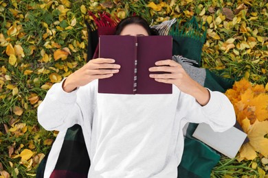 Photo of Woman reading book on grass with dry leaves, above view. Autumn season