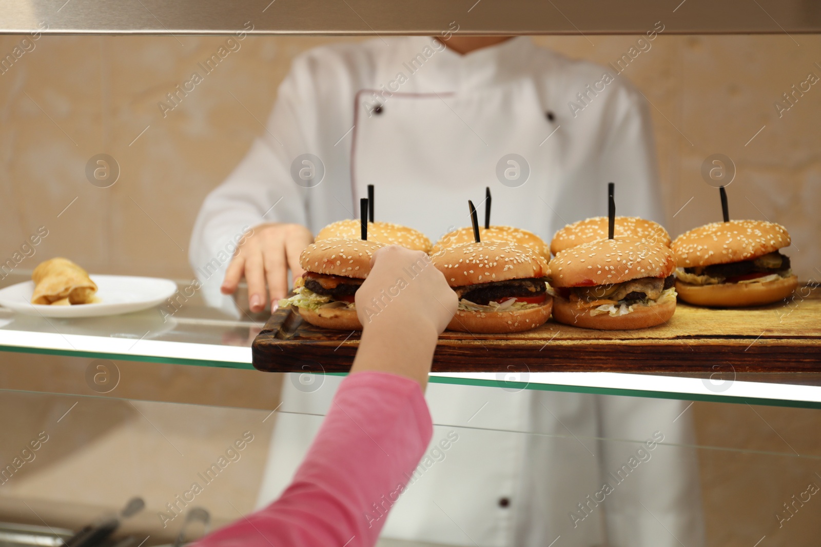 Photo of Little girl taking burger at serving line in canteen. School food
