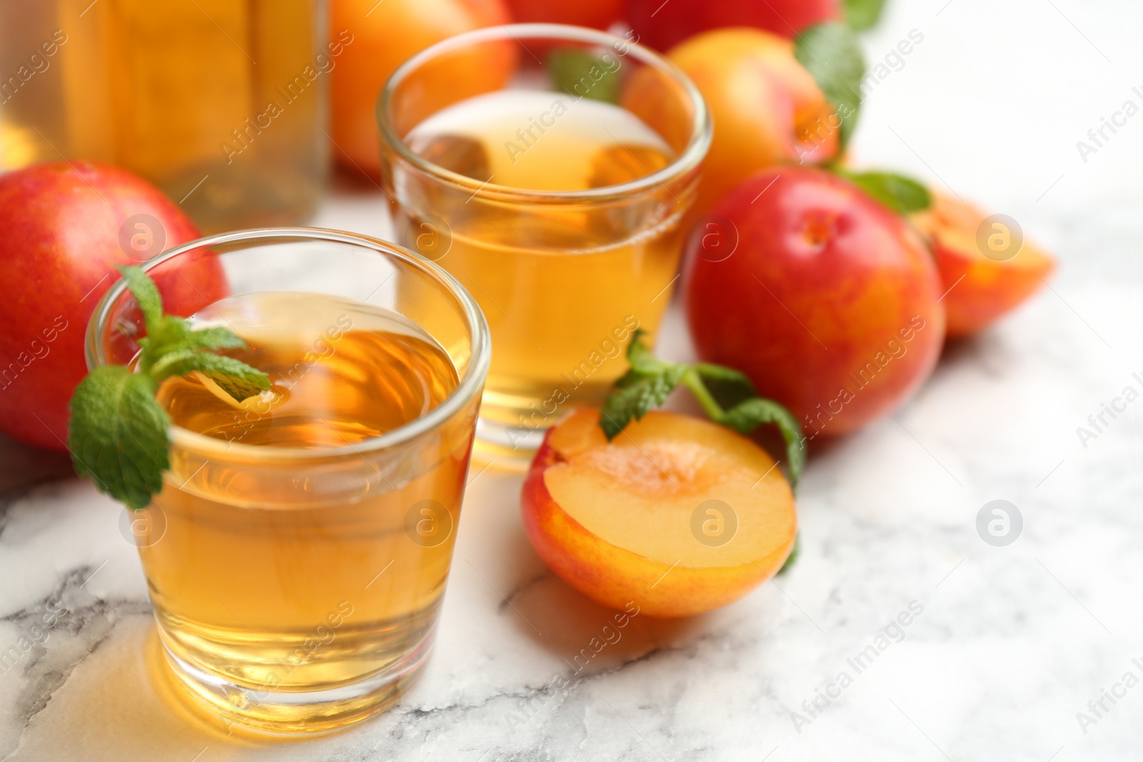 Photo of Delicious plum liquor with mint on white table. Homemade strong alcoholic beverage