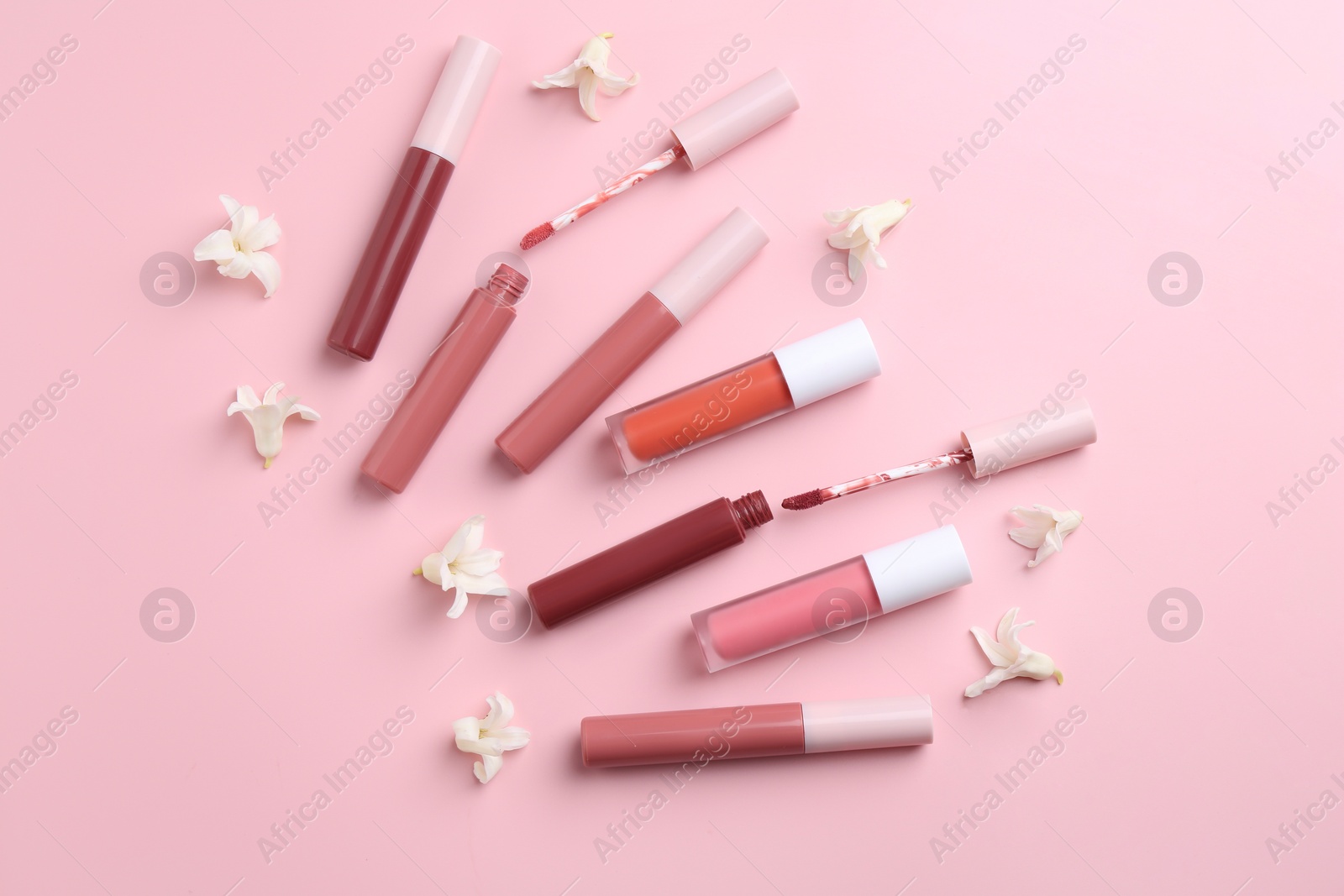 Photo of Different lip glosses, applicators and flowers on pink background, flat lay