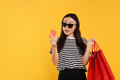 Photo of Happy woman with shopping bags and credit card on yellow background. Space for text