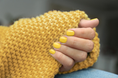 Young woman with stylish yellow manicure and knitted plaid, closeup