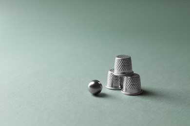 Photo of Metal thimbles and ball on pale olive background, space for text. Thimblerig game