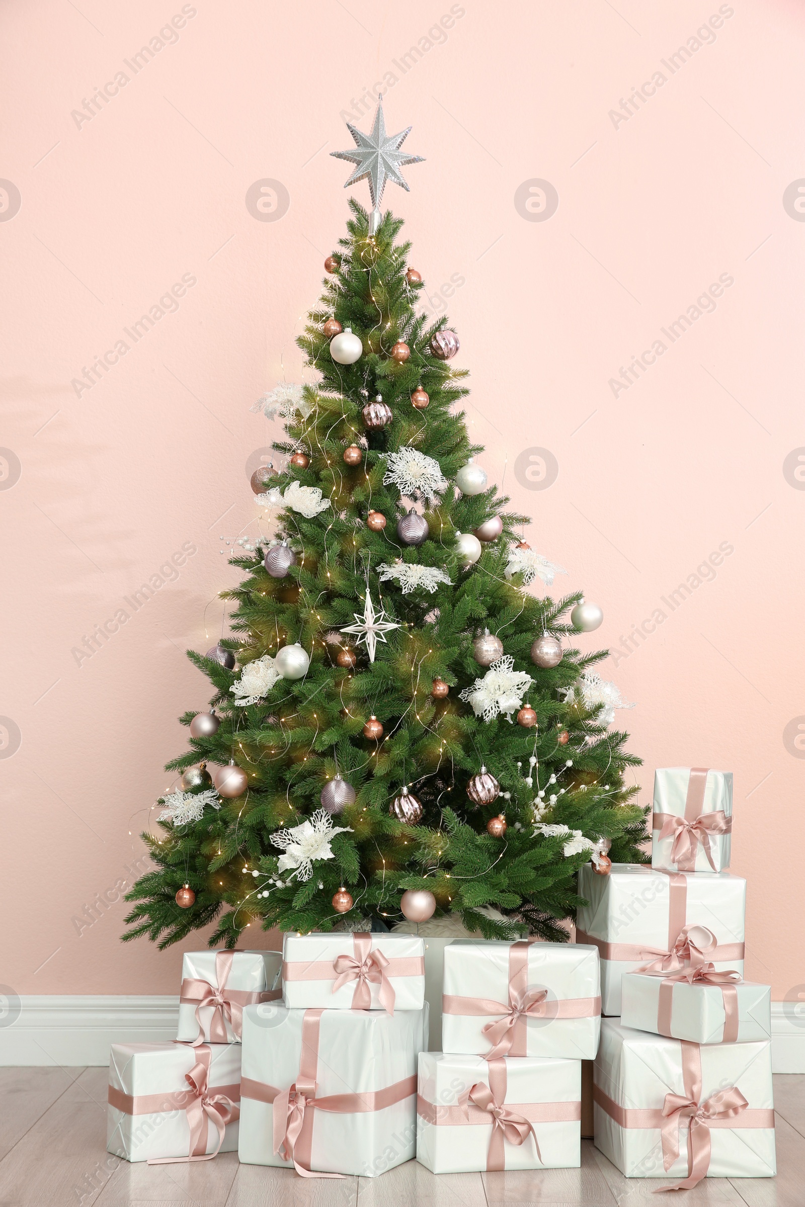 Photo of Beautiful decorated Christmas tree and gifts near pink wall.