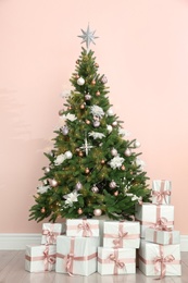 Photo of Beautiful decorated Christmas tree and gifts near pink wall.